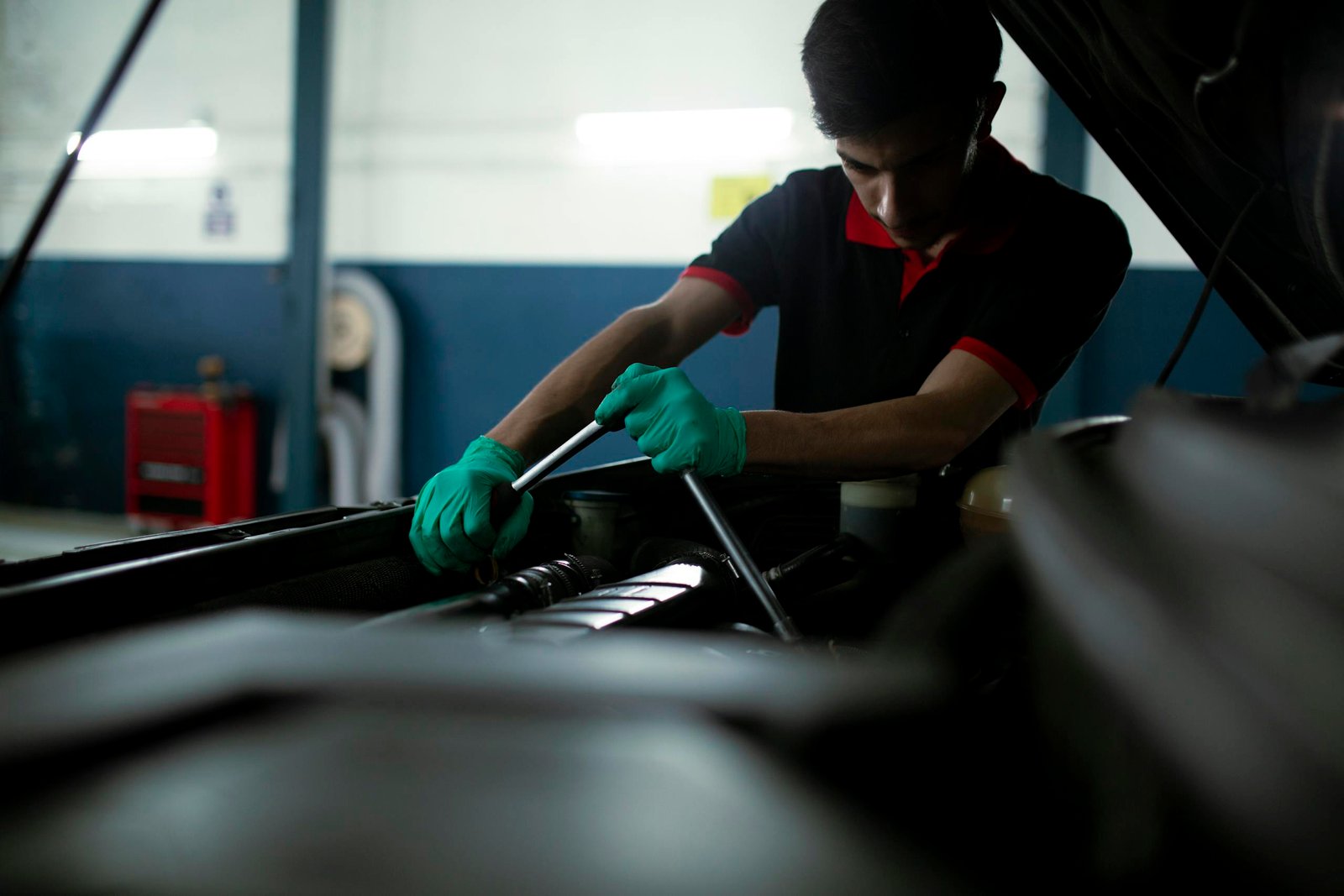 Mechanic wearing gloves using a torque wrench to repair a car engine in an indoor garage.